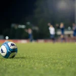 Balón de fútbol sobre el césped con jugadores al fondo