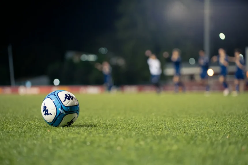 Balón de fútbol sobre el césped con jugadores al fondo