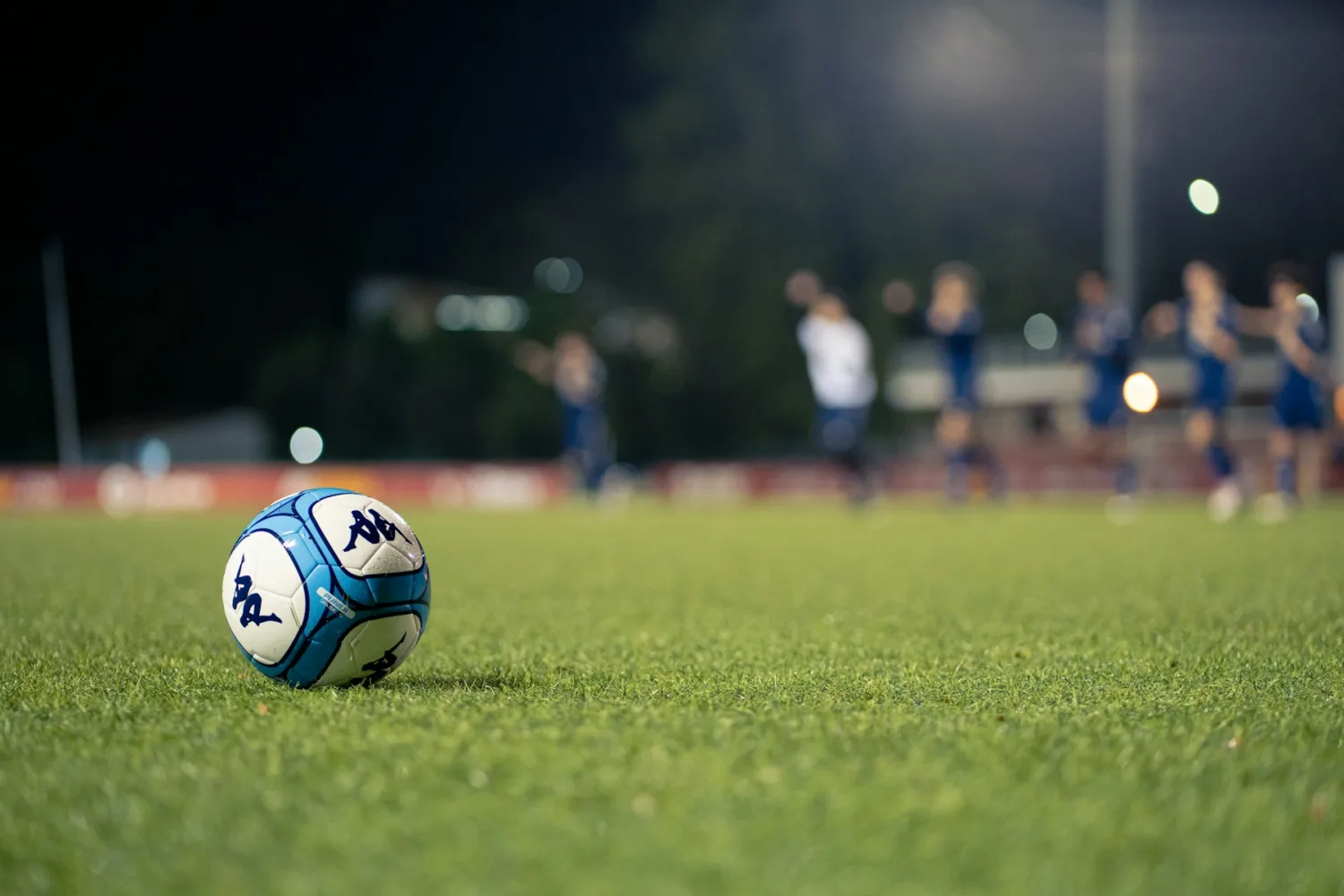 Balón de fútbol sobre el césped con jugadores al fondo